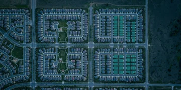 Aerial view of a structured suburban neighborhood at dusk, highlighting geometric patterns of streets and rooftops with green solar panels, symbolizing financial planning and order.